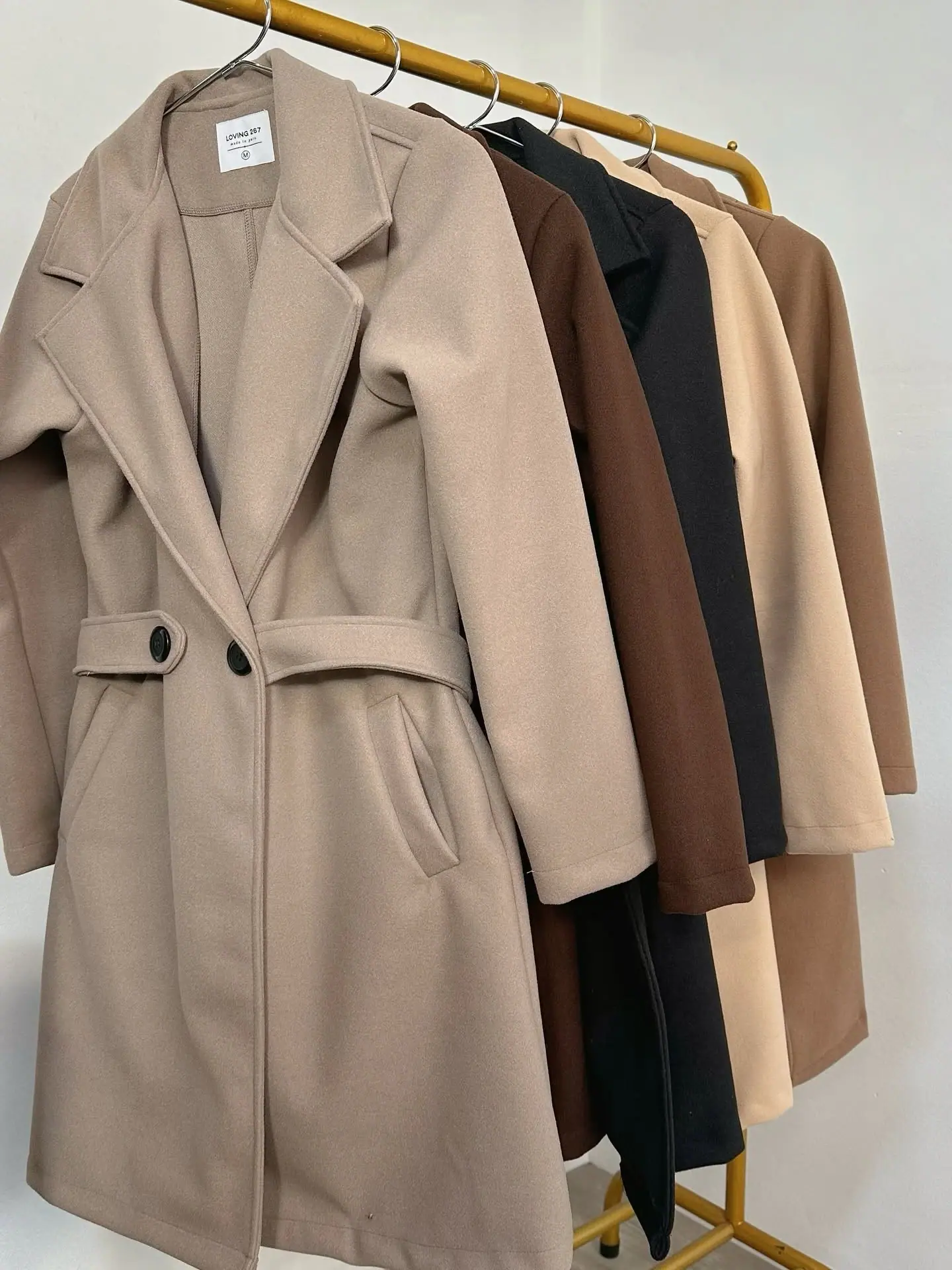 Cinco abrigos con cinturón colgados: topo, chocolate, negro, beige y camel
