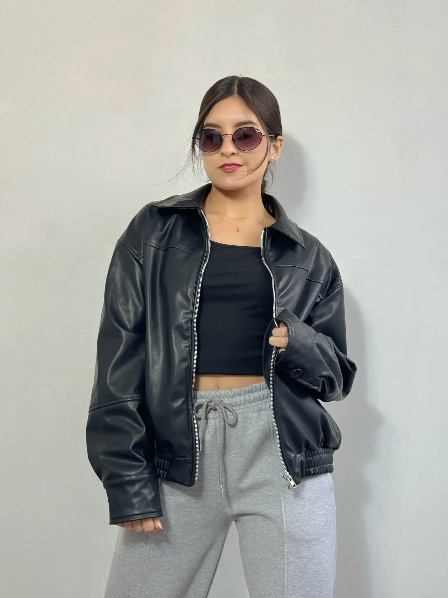 Modelo con bomber negra símil cuero abierta sobre top negro y jogger gris