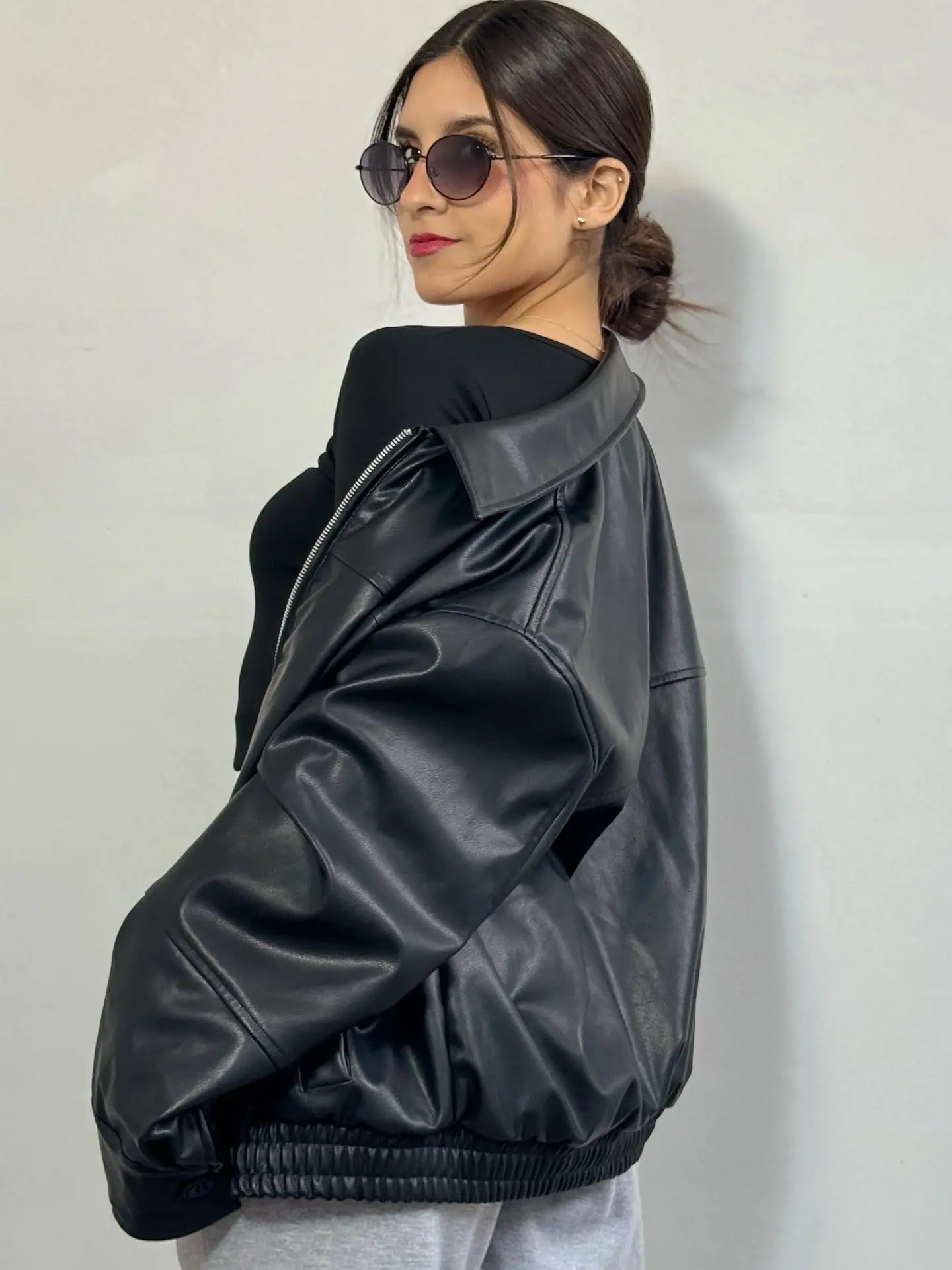 Bomber negra símil cuero vista de perfil, con cuello camisero y basta elástica