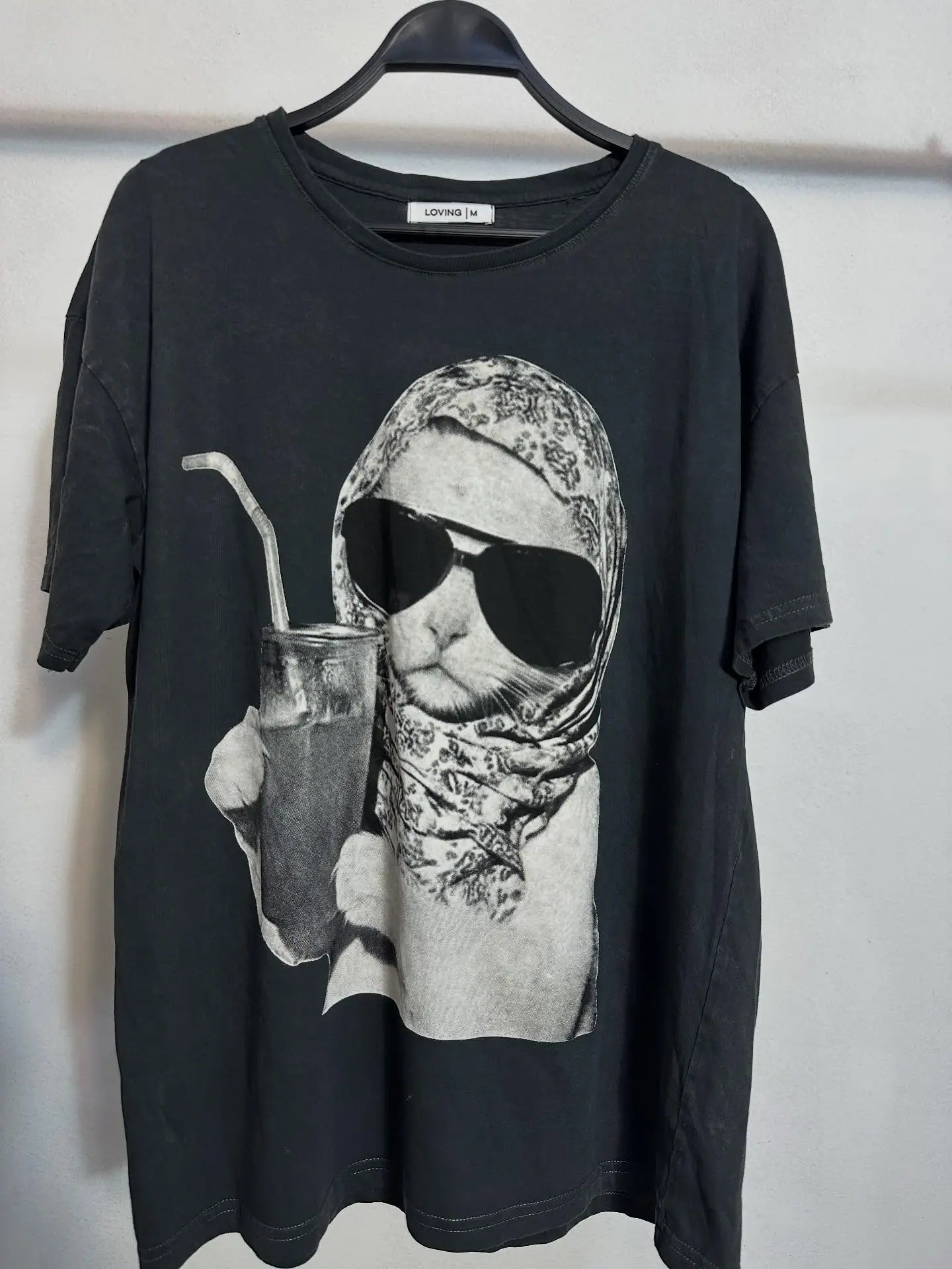 Polo negro lavado con estampado de gato con lentes, pañuelo y vaso con sorbete, colgado