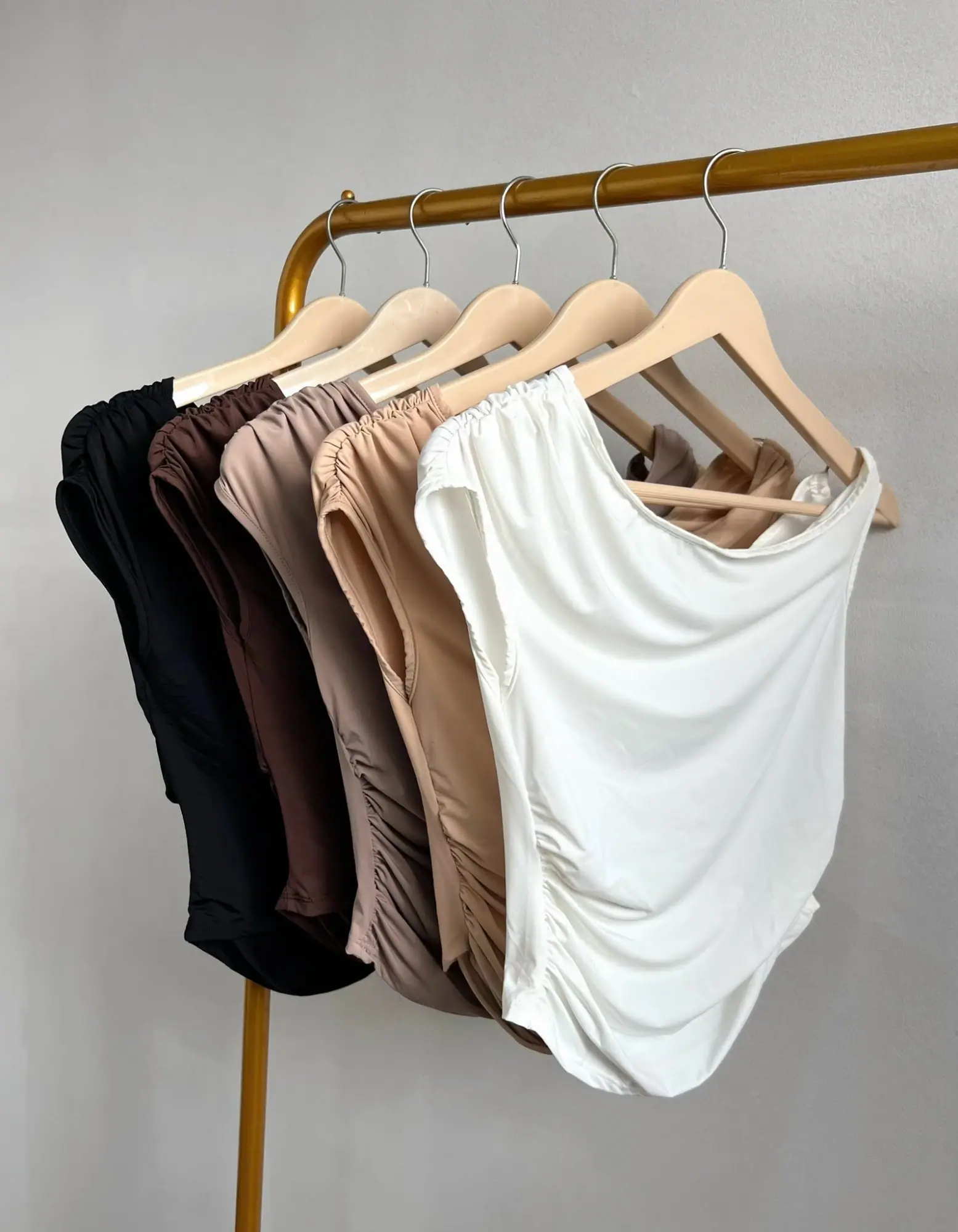 Cinco tops asimétricos colgados: negro, chocolate, topo, camel y blanco